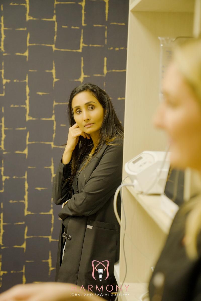 A woman stands behind a counter, looking off to the side with her hand on her chin, while another woman looks at her from across the counter.
