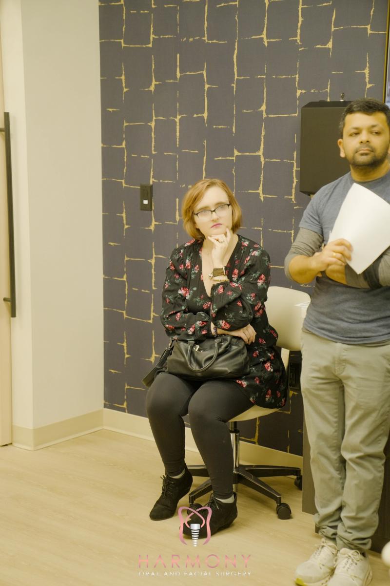 A man and woman in an office setting, with the man standing and holding a paper, and the woman sitting in a wheelchair, both engaged in conversation.
