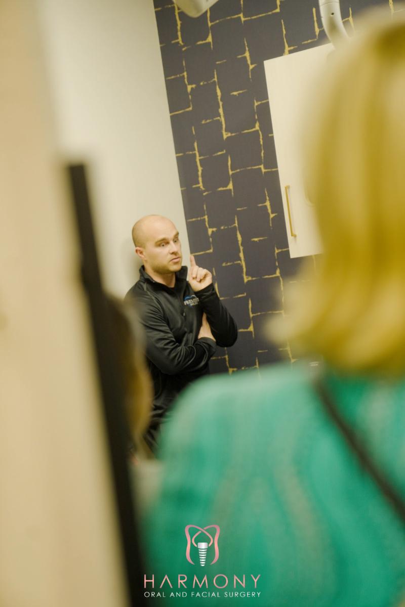 A man standing with his back to the camera, gesturing with his hands, in front of an audience.