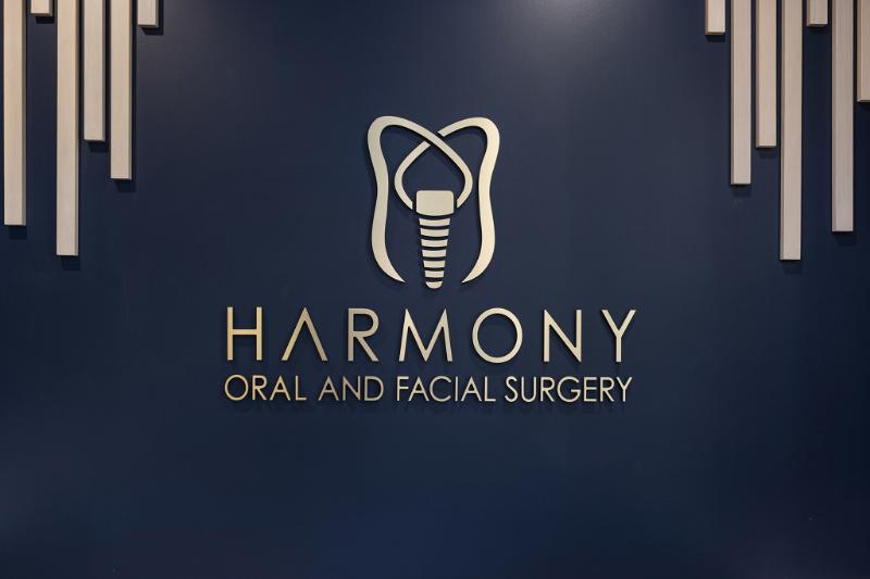 The image displays a sign with the text HARMONY DENTAL AND FACIAL SURGERY against a blue background, featuring a stylized logo and design elements that are likely intended for branding purposes.