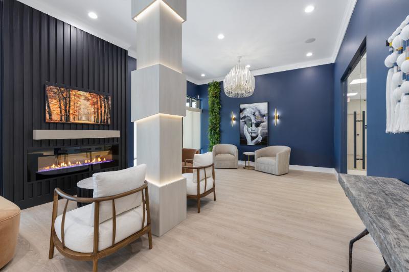 The image shows an interior space with modern furnishings, including a seating area, a fireplace, a television mounted on the wall, and decorative elements such as a painting and plants.