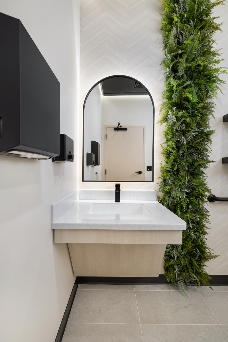 The image depicts a modern bathroom interior with a sink, mirror, and a vertical green plant installation on the wall.