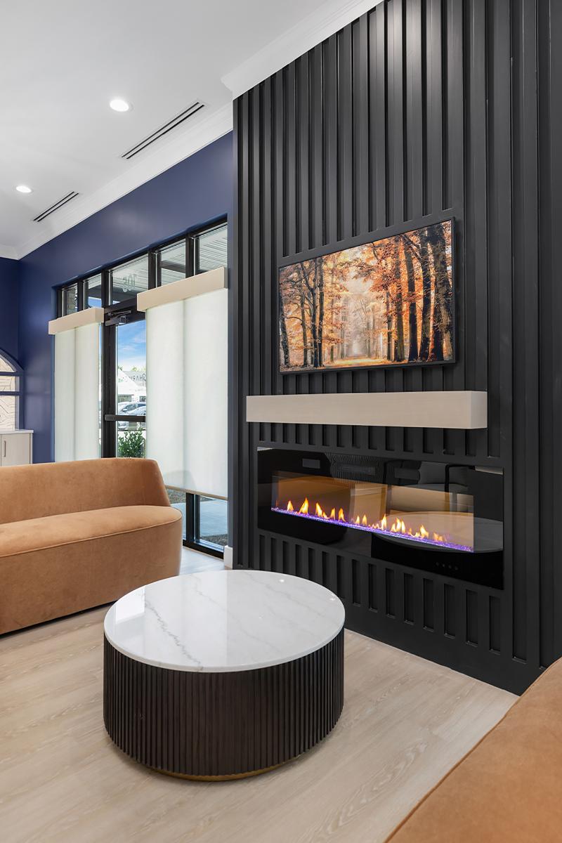 The image shows a modern interior design with a contemporary fireplace and a sleek, dark-toned wall decoration featuring vertical lines and a geometric pattern.