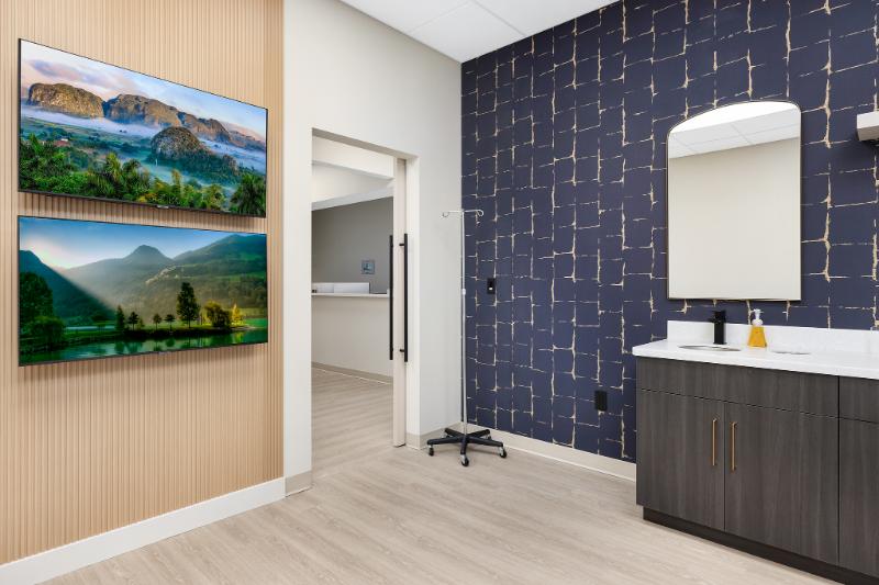 The image shows an interior space that appears to be a waiting room or office with a decorative wall featuring landscape photographs, a modern style desk area, and a large mirror reflecting part of the room.