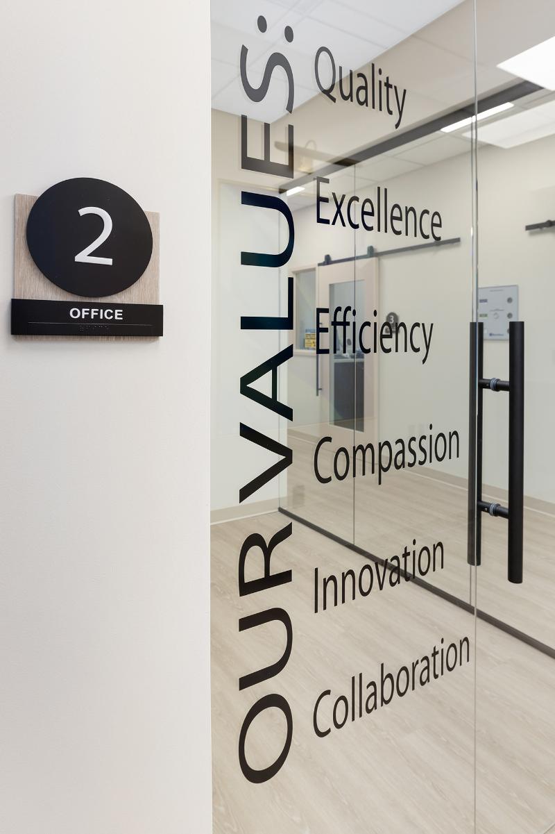 The image shows a glass door with text on it, set against an interior office environment.