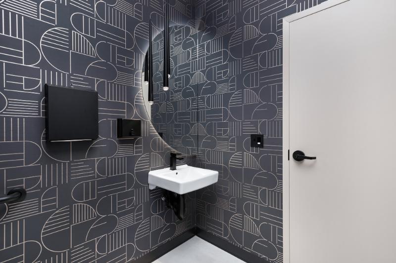 The image shows a modern bathroom with black and white wallpaper featuring geometric designs, including circles and lines, and a mirror above a sink.