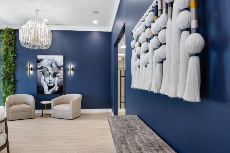 The image shows a modern interior design space with a blue wall, white fur-like decorative elements hanging on the wall, a chandelier, a sofa, and framed artwork.