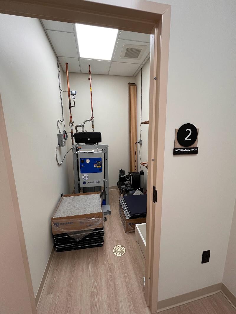 The image shows a narrow hallway leading into an examination room with medical equipment visible on the right side, including a sink and a scale, and a sign indicating this is a '2' on the left wall.