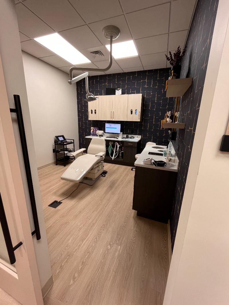 The image shows an interior view of a dental office with a reception area, dental chair, and equipment visible.