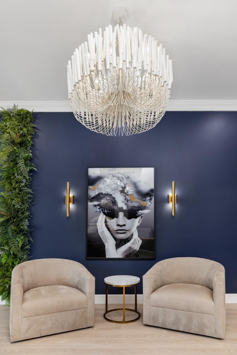 The image shows a modern living room with blue walls, a chandelier, a large abstract art piece on the wall, two chairs, and a sofa.