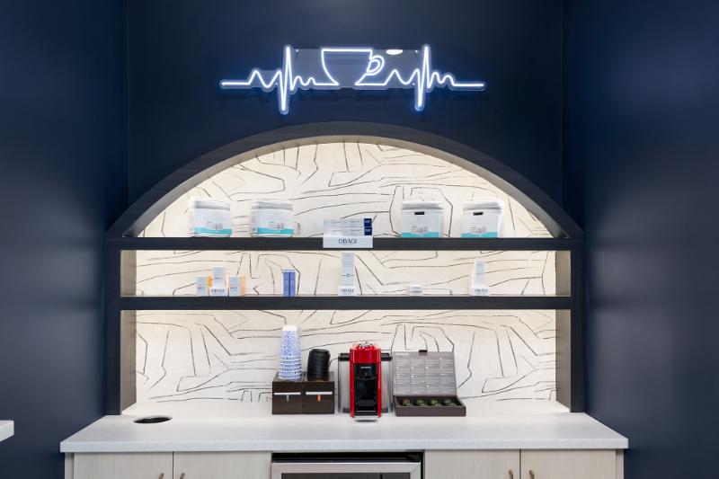The image shows a modern interior space with a curved counter featuring a neon sign that reads 'HEALTH' above it, and various items on shelves behind the counter, suggesting a health-themed store or cafe.