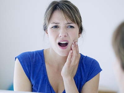 A woman with her mouth open in an expression of surprise or shock, looking at her reflection in a mirror.