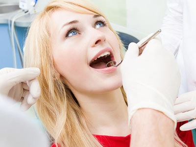 The image shows a woman seated in a dental chair receiving dental treatment from a dentist, with visible dental tools in use.